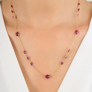 May include: A gold chain necklace with oval-shaped ruby gemstones. The necklace is on a model's neck.