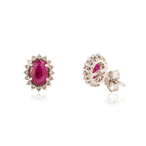 May include: Stud earrings with oval rubies encircled by small diamonds. The earrings have a classic design, suitable for adding a touch of luxury. The gemstones are set in a silver or white gold setting, creating a timeless look.