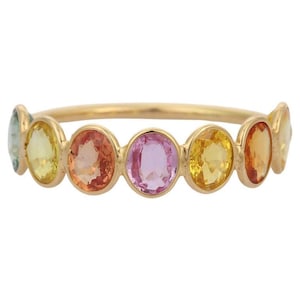 May include: A gold ring with a series of oval gemstones in a rainbow of colours. The gemstones include shades of yellow, orange, pink, and blue. The ring's band is a thin, polished gold.
