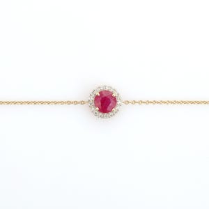 May include: A gold bracelet with a central, round, deep red ruby gemstone encircled by small, clear diamonds. The bracelet has a delicate chain design.