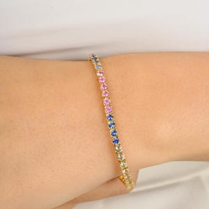 May include: A gold bracelet featuring a row of pink, blue, and clear gemstones. The bracelet is crafted from 14k gold and showcases a classic tennis chain design.
