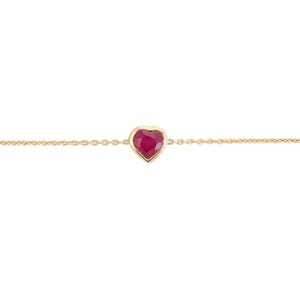Op de afbeelding: Een delicate gouden kettingarmband met een hartvormige robijn edelsteen. De robijn is gezet in een gouden bezel, wat een contrast creëert met de warme gouden ketting. De armband is een eenvoudig maar elegant sieraad.