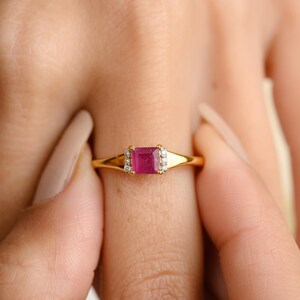 May include: A gold ring with a square-shaped ruby gemstone surrounded by smaller diamonds.