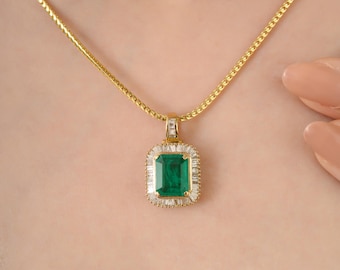 May include: A gold necklace featuring a rectangular emerald pendant. The emerald is surrounded by a halo of small, clear gemstones. The chain is a delicate gold link design, and the necklace is displayed on a person's neck.