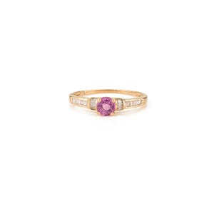 May include: A gold ring featuring a round, pink gemstone center with smaller, rectangular white gemstones on either side. The ring has a delicate band and is set against a white background.