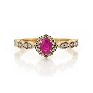 May include: A gold ring featuring a central oval-cut vibrant pink ruby surrounded by a halo of small round white diamonds. The band is crafted from yellow gold and includes additional diamond accents set in a decorative, scalloped metal frame.