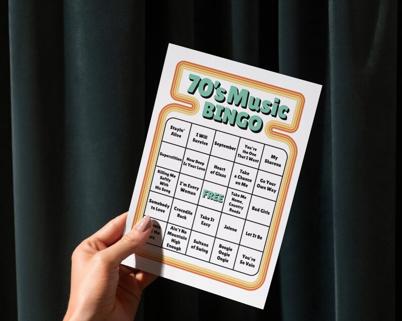 May include: A retro-style bingo card with the text "70's Music BINGO" in a teal and orange design. The card features a grid of song titles from the 1970s. The card is held by a hand against a dark green background.
