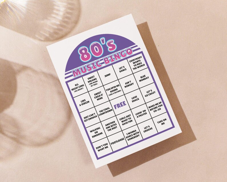 May include: A white 80's Music Bingo card with a purple and pink header. The bingo card features song titles from the 1980s, including "Sweet Dreams" and "Like a Virgin". The card is on a brown envelope.