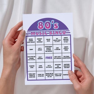 May include: A white 80's Music Bingo card with a purple and pink header. The card features a grid of song titles like "Hungry Like the Wolf" and "Sweet Dreams." The card is held by a person.