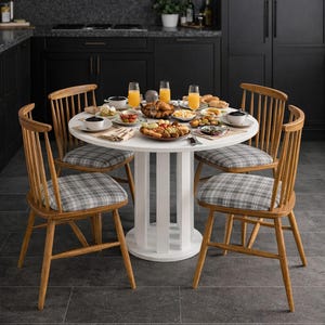 Puede incluir: Una mesa de comedor redonda y blanca, preparada para una comida, rodeada de cuatro sillas de madera con cojines de asiento a cuadros. La mesa está cargada de comida y bebidas, incluido zumo de naranja en vasos. La cocina tiene armarios oscuros.