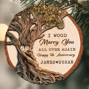 Op de afbeelding: Een houten kerstornament met een boomontwerp en de tekst "I WOOD Marry You All Over Again Happy 5th Anniversary JAMES SUSAN". Het ornament heeft een natuurlijke houtnerf en een gouden draad om op te hangen.