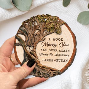 Op de afbeelding: Houten boomschijf ornament met een uitgesneden boomontwerp en de tekst "I Wood Marry You All Over Again Happy 5th Anniversary James & Susan". Het ornament is rond en heeft een natuurlijke houtnerf.