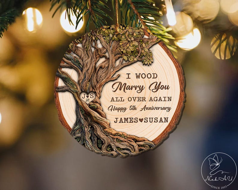 Op de afbeelding: Ronde houten ornament met een boomontwerp en de tekst "I Wood Marry You All Over Again Happy 5th Anniversary JAMES SUSAN". Het ornament heeft een bruine schorsrand en een gouden touwtje om op te hangen.