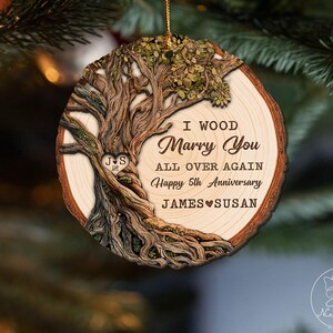 Op de afbeelding: Houten kerstornament met een boomontwerp en de tekst "I Wood Marry You All Over Again Happy 5th Anniversary JAMES SUSAN". Het ornament heeft een natuurlijke houtnerf en een gouden touwtje om op te hangen.