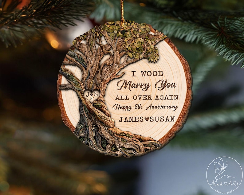 Op de afbeelding: Houten kerstornament met een boomontwerp en de tekst "I Wood Marry You All Over Again Happy 5th Anniversary JAMES SUSAN". Het ornament heeft een natuurlijke houtnerf en een gouden touwtje om op te hangen.
