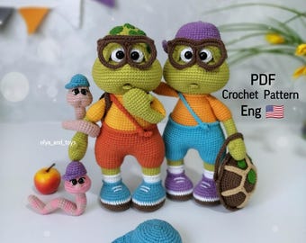 Puede incluir: Patrón de crochet para dos tortugas verdes que llevan gafas y llevan una mochila y una bolsa. Las tortugas llevan pantalones cortos naranja y azules. El patrón está en inglés.
