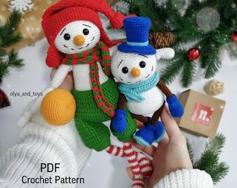 Könnte beinhalten: Zwei gehäkelte Schneemänner, einer mit roter Mütze und grüner Hose, der andere mit blauem Zylinder und blauen Stiefeln. Beide haben Karottennasen und schwarze Augen. Der Text "PDF Crochet Pattern Eng" ist sichtbar.