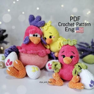 May include: Crochet pattern for three amigurumi chicks. One chick is pink with purple accents, one is yellow, and one is pink with green accents. Each chick is holding a white crocheted egg. The pattern is available in English. PDF Crochet Pattern Eng.