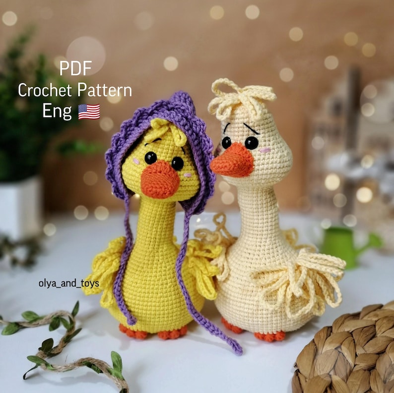 May include: Two crocheted goose amigurumi toys. One goose is yellow with a purple crocheted hat. The other goose is a light yellow color. Both geese have black eyes and orange beaks. The text "PDF Crochet Pattern Eng" is visible in the image.