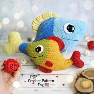 May include: Crochet pattern for two amigurumi fish toys. One fish is blue and yellow, the other is green, yellow, and red. The pattern is available in English.