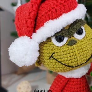 Puede incluir: Mu&ntilde;eco Grinch tejido a ganchillo, con gorro de Pap&aacute; Noel rojo con ribete blanco. El Grinch es verde, con un atuendo rojo y ojos negros. El mu&ntilde;eco tiene una sonrisa cosida, ideal para decoraciones navide&ntilde;as.