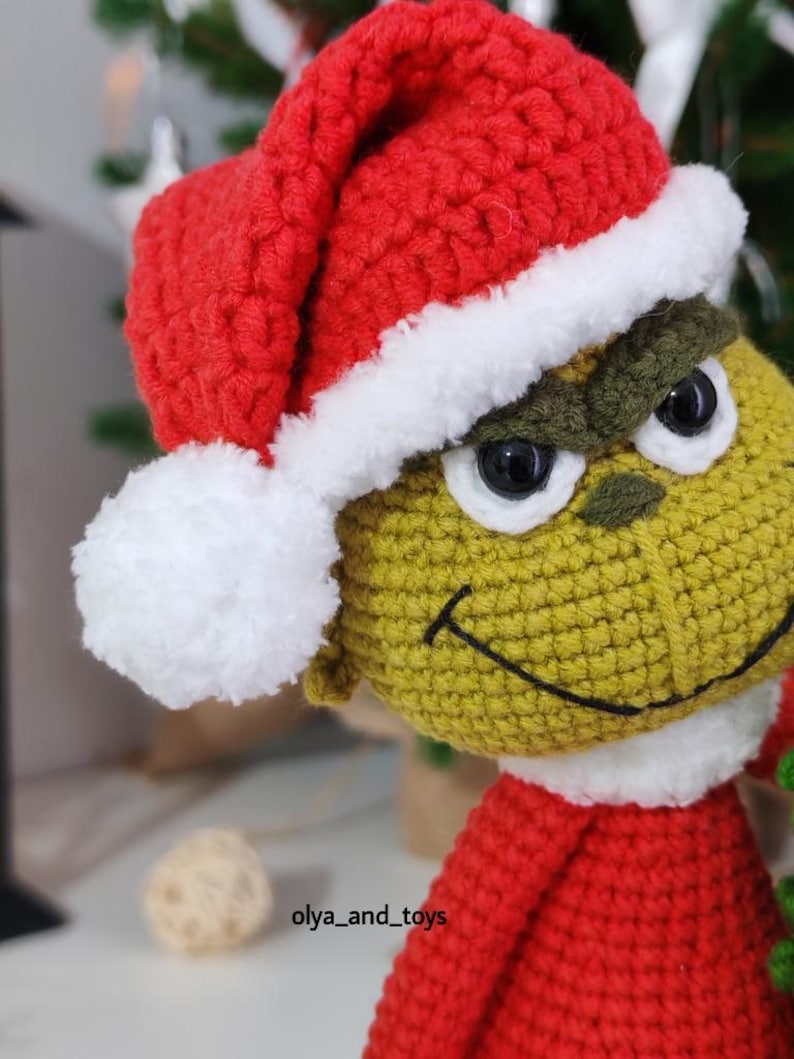 Puede incluir: Mu&ntilde;eco Grinch tejido a ganchillo, con gorro de Pap&aacute; Noel rojo con ribete blanco. El Grinch es verde, con un atuendo rojo y ojos negros. El mu&ntilde;eco tiene una sonrisa cosida, ideal para decoraciones navide&ntilde;as.