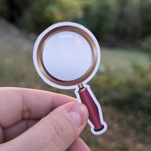 May include: A magnifying glass sticker with a gold frame and a red handle.