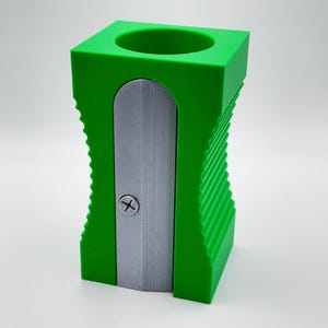 May include: A green plastic pencil sharpener with a silver blade. The sharpener has a ribbed design and a small hole on the top for holding pencils.