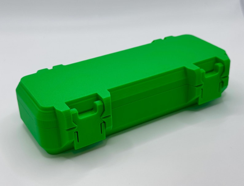 K&ouml;nnte beinhalten: Eine leuchtend gr&uuml;ne, rechteckige Box mit einem Klappdeckel und zwei sicheren Verschl&uuml;ssen. Die Box besteht aus einem soliden, haltbaren Material und ist zum Schutz des Inhalts konzipiert. Die Box wird vor einem wei&szlig;en Hintergrund gezeigt.