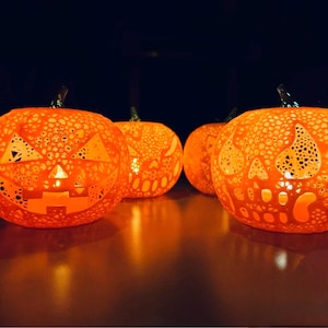 May include: Four illuminated orange carved pumpkins with jack-o'-lantern faces. The pumpkins have a textured surface and are lit from within, creating a warm glow. The pumpkins are arranged in a row, perfect for Halloween.