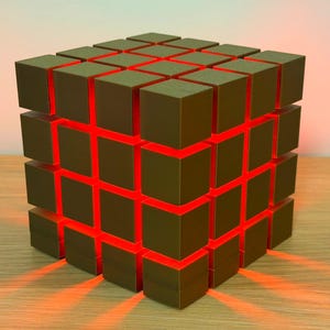 以下が含まれることがあります： 茶色のブロックのグリッドを持つ、幾何学的な立方体型のランプ。ブロック間の空間は明るい赤色に光ります。ランプは木製の表面に置かれ、暖かい赤い光を放っています。