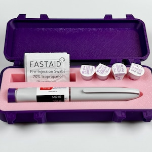 K&ouml;nnte beinhalten: Ein offener, violetter Koffer mit einem wei&szlig;en und grauen medizinischen Stift, Vorinjektions-Tupfern und vier kleinen Fl&auml;schchen. Das Innere ist rosa. Der Stift hat eine violette Spitze. Die Tupfer sind mit "FASTAID" beschriftet.