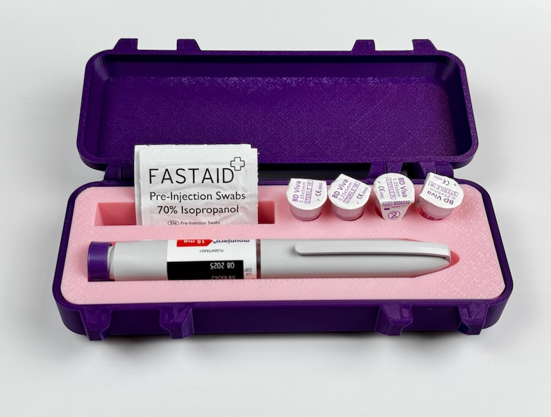 K&ouml;nnte beinhalten: Ein offener, violetter Koffer mit einem wei&szlig;en und grauen medizinischen Stift, Vorinjektions-Tupfern und vier kleinen Fl&auml;schchen. Das Innere ist rosa. Der Stift hat eine violette Spitze. Die Tupfer sind mit "FASTAID" beschriftet.