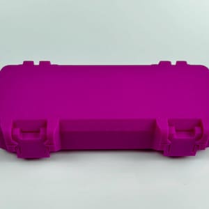 K&ouml;nnte beinhalten: Ein magentafarbener rechteckiger Koffer mit zwei sicheren Verschl&uuml;ssen und einem Klappdeckel. Der Koffer besteht aus einem soliden, langlebigen Material und ist zum Schutz seines Inhalts konzipiert. Der Koffer wird auf wei&szlig;em Hintergrund gezeigt.