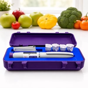 Könnte beinhalten: Ein lila Etui mit blauem Innenraum enthält einen weißen und grauen medizinischen Stift, vier kleine Fläschchen und andere medizinische Utensilien. Das Etui ist geöffnet. Frisches Obst und Gemüse befinden sich im Hintergrund.
