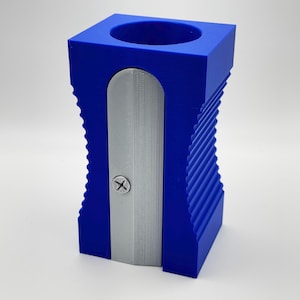 May include: A blue plastic pencil sharpener with a silver blade. The sharpener has a ribbed design and a small hole for collecting pencil shavings.