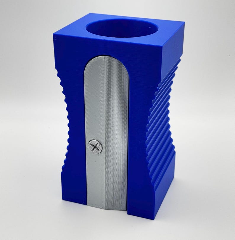 May include: A blue plastic pencil sharpener with a silver blade. The sharpener has a ribbed design and a small hole for collecting pencil shavings.