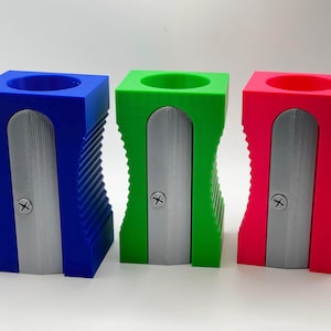 May include: Three pencil sharpeners in blue, green, and pink. Each sharpener has a silver blade and a ribbed design.