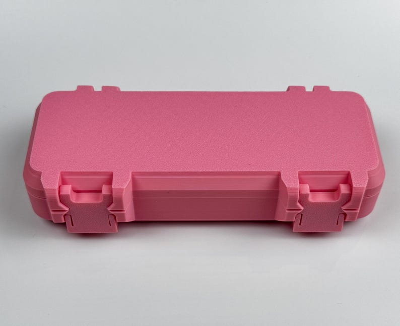 K&ouml;nnte beinhalten: Ein rosa rechteckiger Koffer mit strukturierter Oberfl&auml;che. Der Koffer hat zwei Verschl&uuml;sse vorne und zwei hinten. Der Koffer ist geschlossen und liegt auf einer wei&szlig;en Oberfl&auml;che.