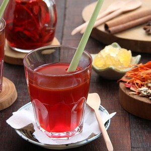 May include: Two glasses of red liquid with straws, a wooden cutting board with cinnamon sticks, star anise, and sugar cubes, and a bowl of dried ginger and turmeric.