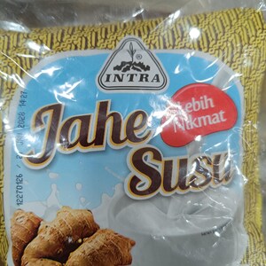 Puede incluir: Un paquete de Jahe Susu, una bebida de leche y jengibre, de la marca Intra. El envase presenta un fondo azul claro con la inscripción "Jahe Susu" en marrón y una imagen de raíces de jengibre. Una burbuja roja dice "Lebih Nikmat".