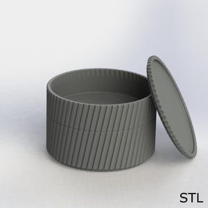 以下が含まれることがあります： グレーの円筒形の容器と蓋。容器は、リブ付きのテクスチャ加工された外観と、わずかに開いたお揃いの蓋を備えています。 デザインはモダンでミニマルで、保管やディスプレイに適しています。 テキスト「STL」が右下に表示されています。