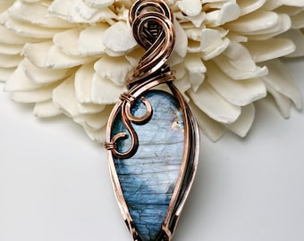 Peut inclure: Un pendentif en forme de larme avec une pierre de labradorite bleue et blanche enveloppée de fil de cuivre.