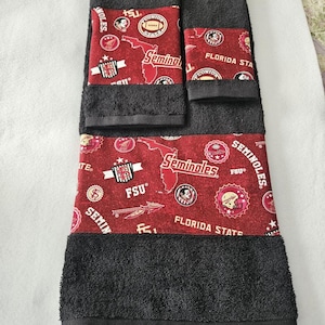 May include: A set of three black towels with a red and gold Florida State Seminoles themed border. The border features the team logo, mascot, and the words "Seminoles" and "Florida State".