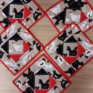 Puede incluir: Cinco posavasos cuadrados con borde rojo. Cada posavasos presenta un diseño de patchwork de pollos negros y blancos sobre una tela de lino beige.
