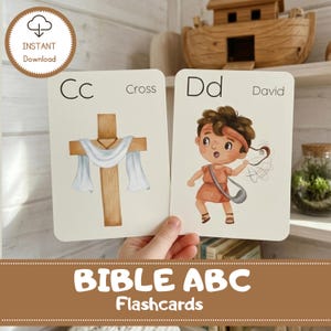 May include: Two Bible ABC flashcards with illustrations. One card shows a wooden cross with a white cloth, labeled "Cc Cross." The other card depicts a cartoon boy with a sling, labeled "Dd David." The words "BIBLE ABC Flashcards" are at the bottom.