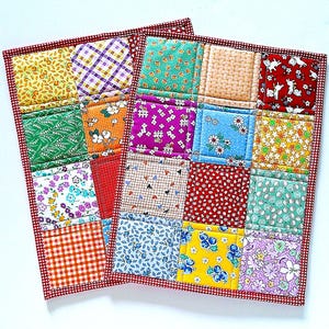 May include: Two handmade quilted pot holders with a patchwork design. Each pot holder features a red gingham border and a grid of colorful fabric squares with floral, geometric, and patterned prints. The pot holders are designed for kitchen use.