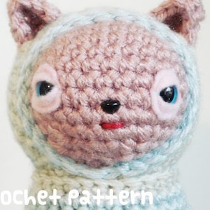 May include: A crocheted amigurumi cat toy with blue and pink accents. The cat has large eyes and a pink nose. The cat is wearing a blue and white crocheted hat.