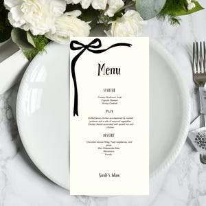 May include: A cream-colored menu card with black text and a decorative bow design. The menu lists starters, main courses, and desserts, including Creamy Mushroom Soup and Chocolate mousse filling. The names "Sarah & Adam" are at the bottom.