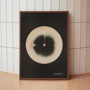 May include: Abstract art print in a dark wooden frame. The artwork features a large, off-white circular shape with a central point of light against a black background. The print includes text at the bottom.
